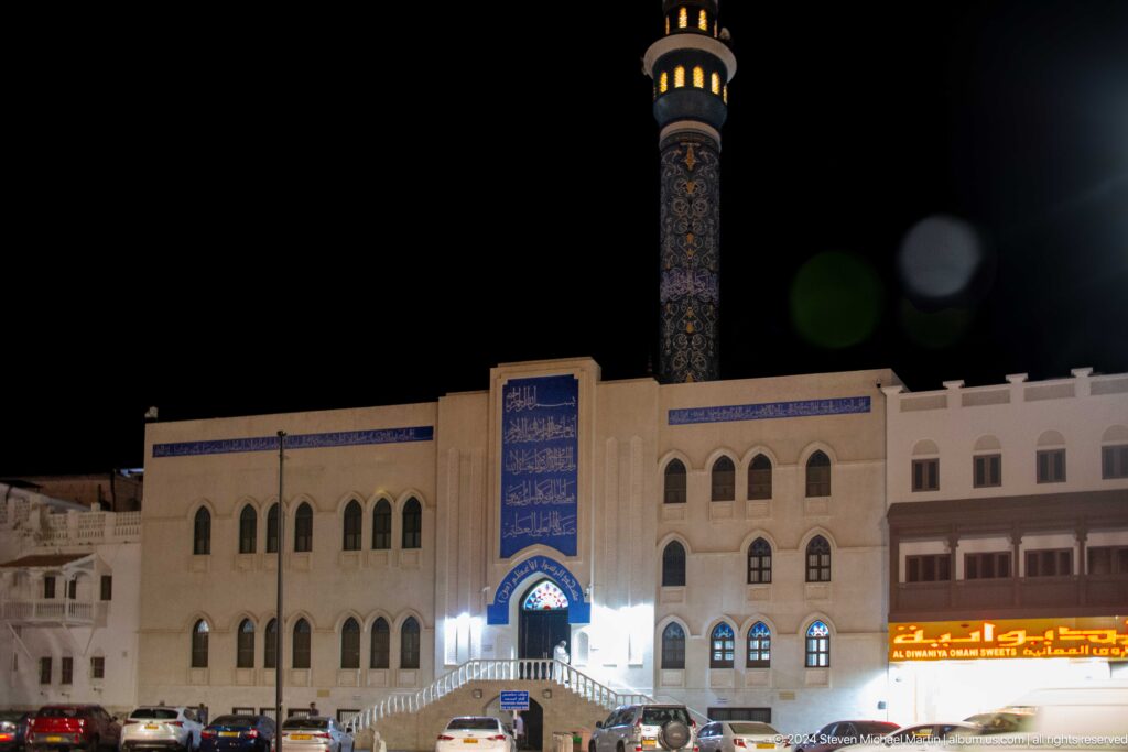 White waterfront building and tall decorated minaret at night.