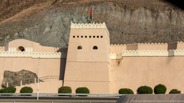 Sand-colored crenellated wall and square tower.