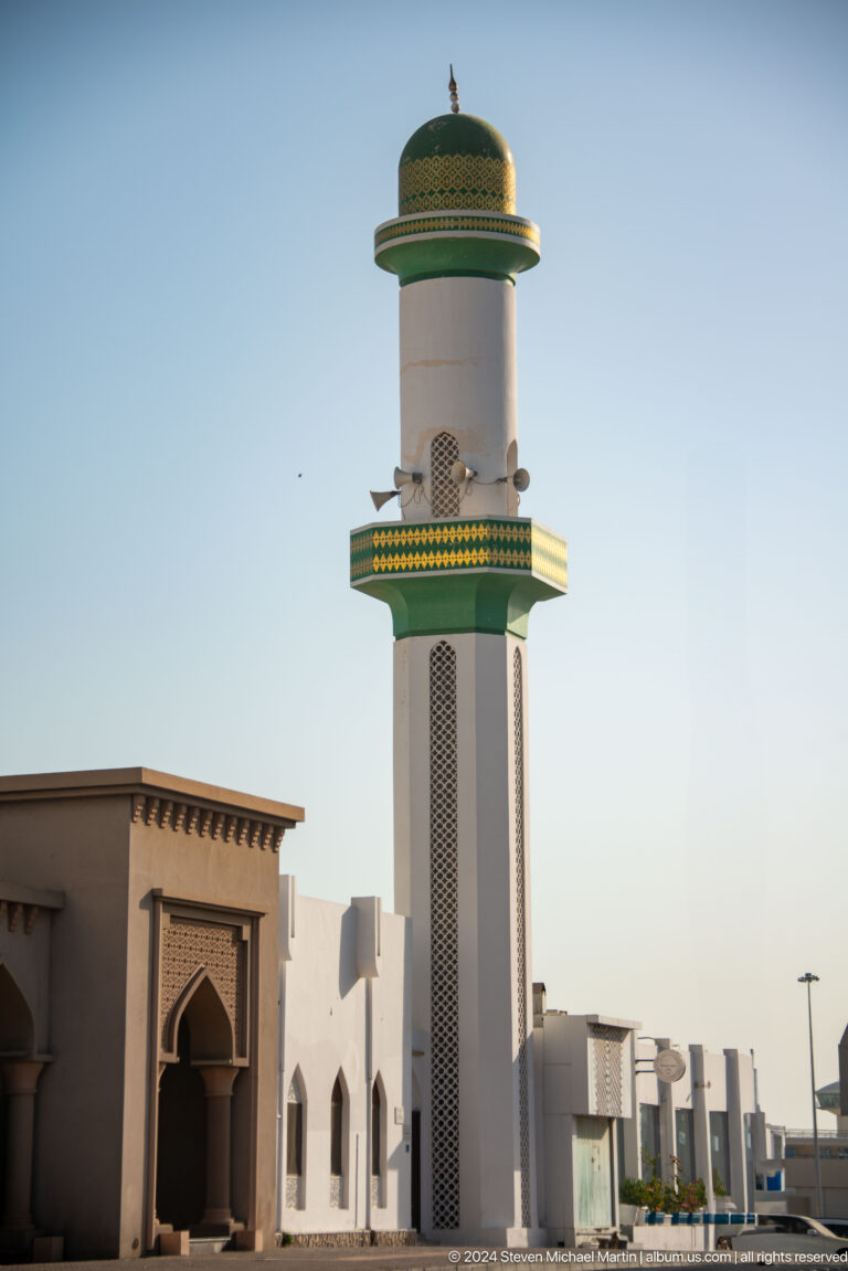 White and green minaret against clear sky.