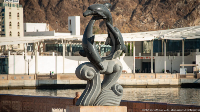 Large silver fish sculpture on wave-shaped base.