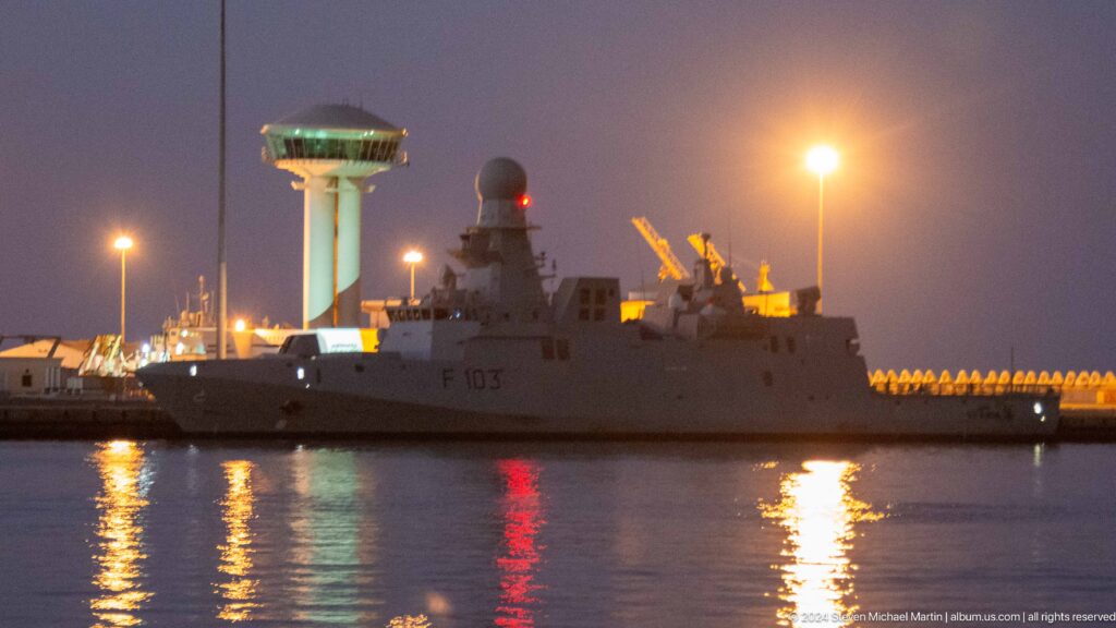 Large ship illuminated beside port infrastructure at night.
