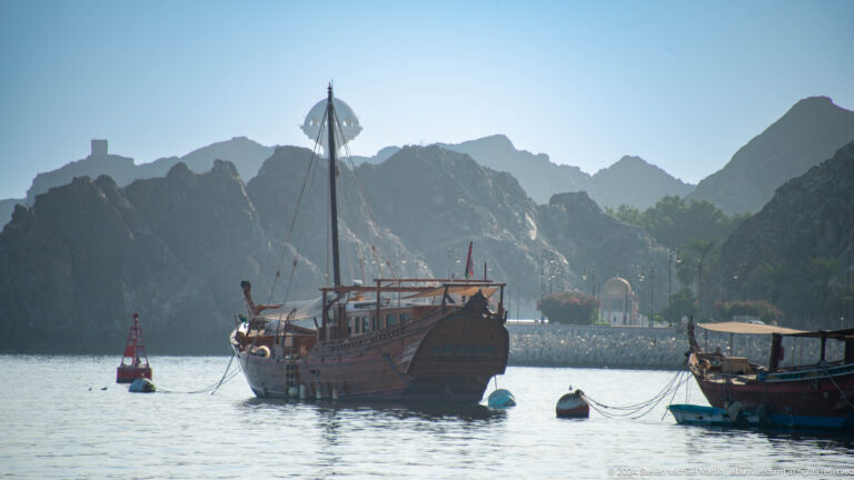 Wooden dhow anchored in harbor against mountains.