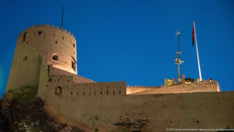 Stone fort wall and round tower under evening sky.