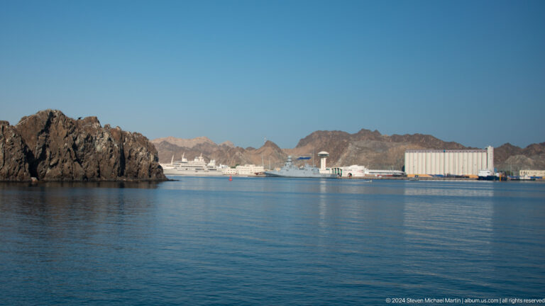 Calm harbor with rocky headland and white buildings.