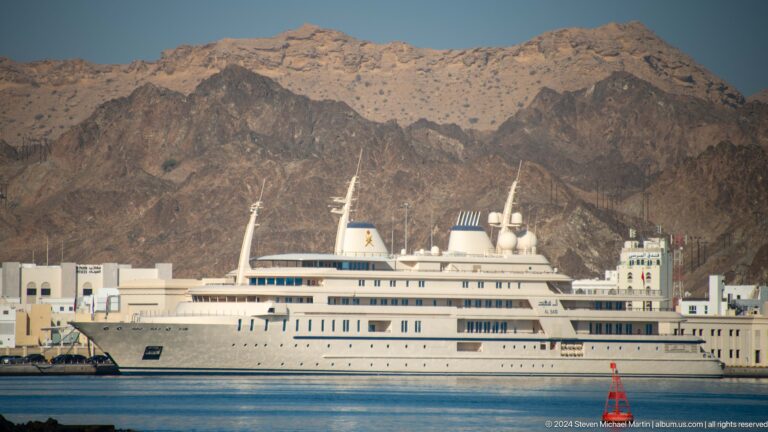 Large white passenger yacht against mountains.