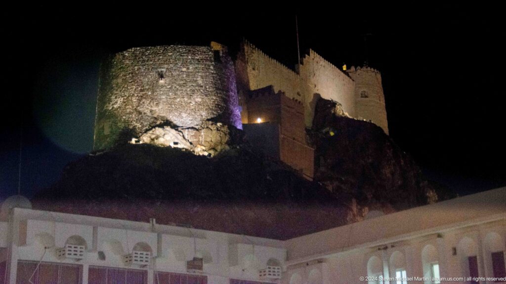 Fort complex illuminated on rocky hill at night.