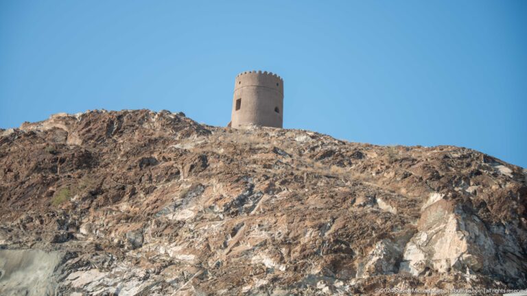 Isolated cylindrical watchtower on barren ridge.