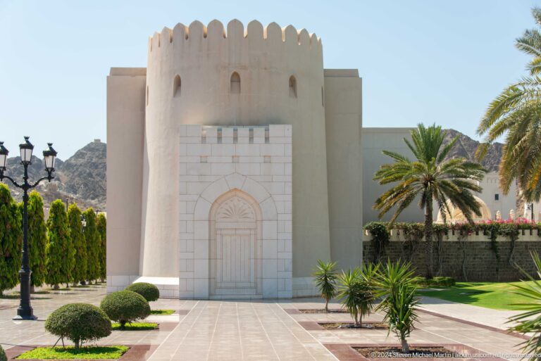 Square crenellated gateway tower among palms.