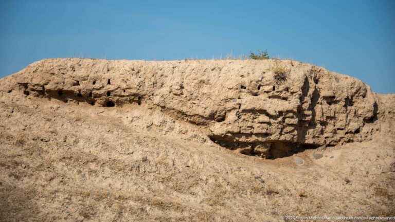 Close-up of a weathered mud-brick wall at Ancient Panjakent, showing layered earthen fabric with rounded, undercut erosion cavities.