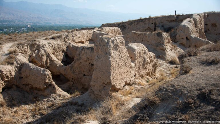 Wide view of eroded mud-brick wall stubs forming shallow, irregular room-like spaces at the Ancient Panjakent archaeological site.