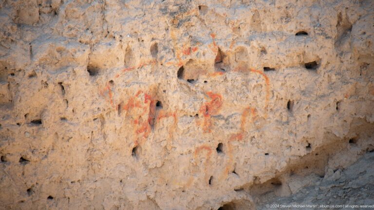 Close view of a weathered plaster wall at Ancient Panjakent with faint red pigment traces and small surface cavities.