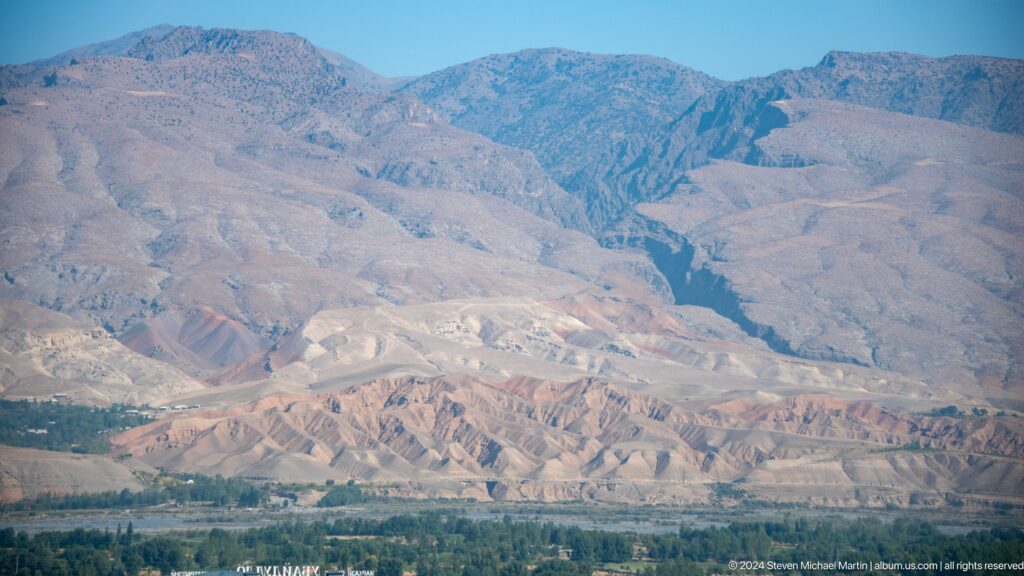 View of multicolored, folded mountain slopes and a deep ravine bordering a green valley edge near Panjakent.