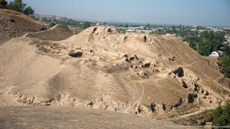 Elevated view of a large, eroded archaeological mound at Ancient Panjakent, showing cavities and footpaths across the layered earthen ruins.
