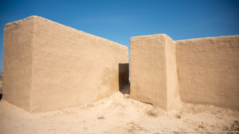 Conserved mud-brick wall junction at Ancient Panjakent, with a narrow passage between thick earthen walls and a smooth protective coating contrasting with rough, eroded surfaces.