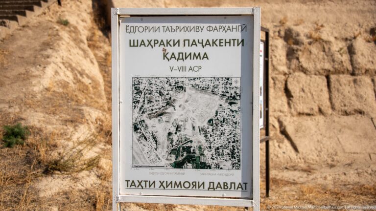 Close view of the official state-protected monument sign for Ancient Panjakent, showing an aerial image of the site and text dating the ancient city to the fifth–eighth centuries.