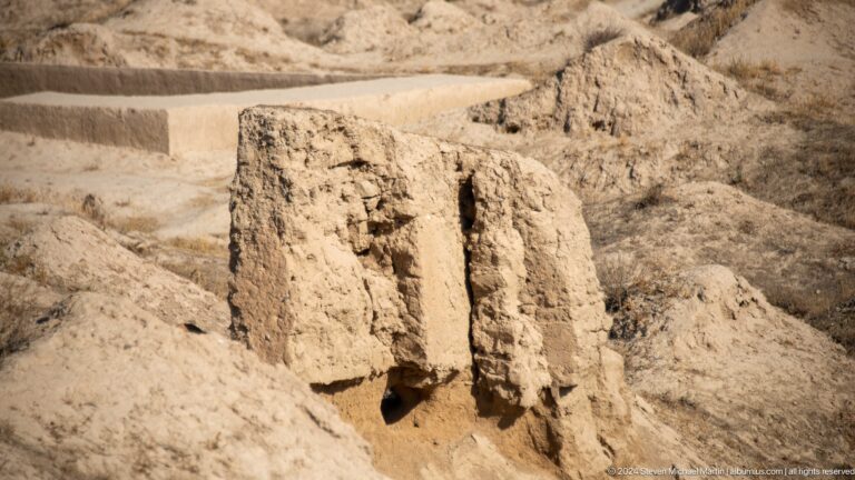 Close view of a heavily eroded mud-brick wall remnant with recessed sections and a small opening at its base within the ruins of Ancient Panjakent.