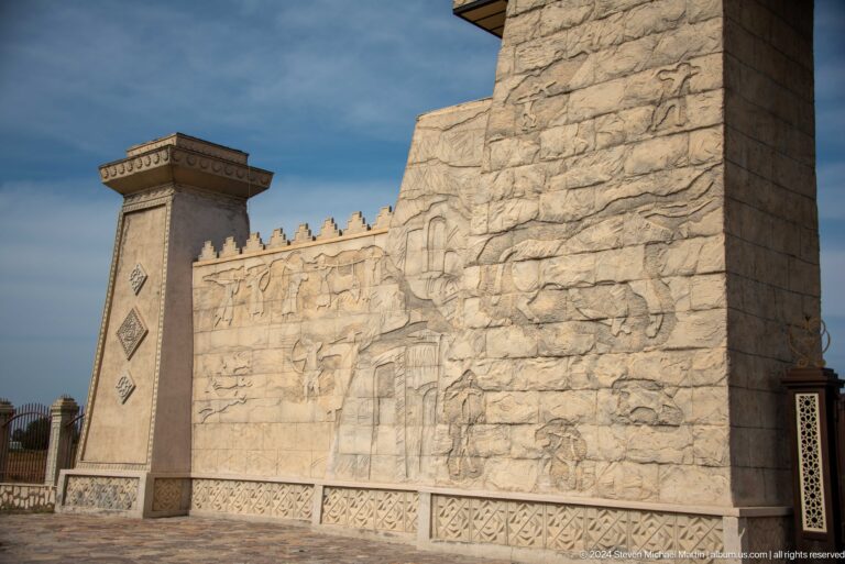 Angled view of a pale stone entrance wall at Ancient Sarazm with linear carved relief extending across the facade.