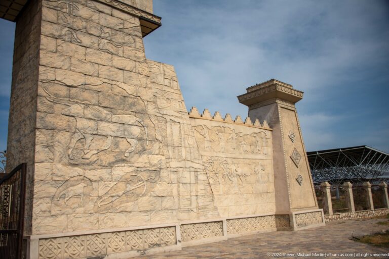 Long pale stone perimeter wall at the Sarazm entrance with a projecting corner pier and shallow relief decoration along the upper section.