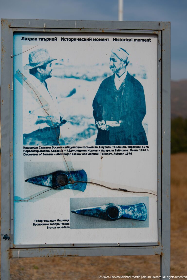 Interpretive panel at Sarazm displaying photographs of excavated artifacts, including dark stone and metal pieces that appear to be tools and ornaments.