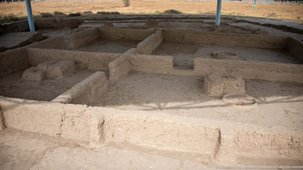 Excavated mud-brick room complex at Ancient Sarazm with straight low earthen walls forming adjacent compartments under a shelter.