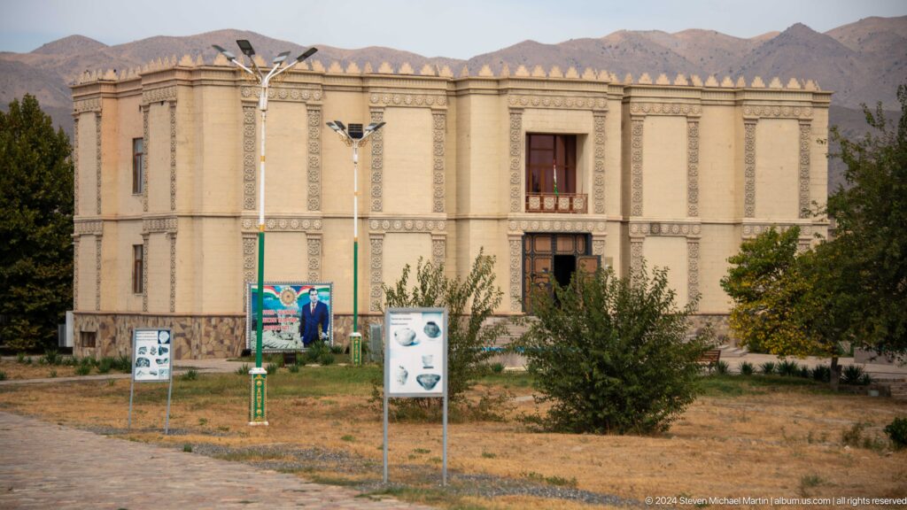 Museum complex at Ancient Sarazm in Tajikistan with a symmetrical facade, recessed central entrance, and mountain ridges in the background.