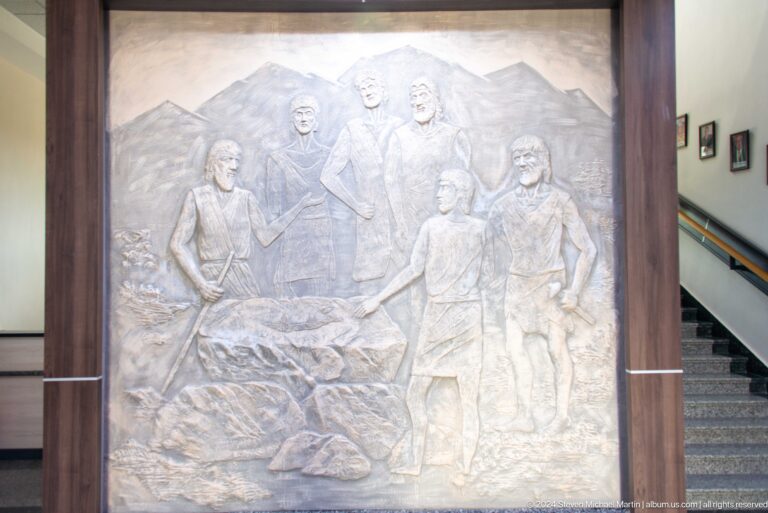 Large stone relief at Sarazm showing several human figures in low relief, including seated and standing workers.