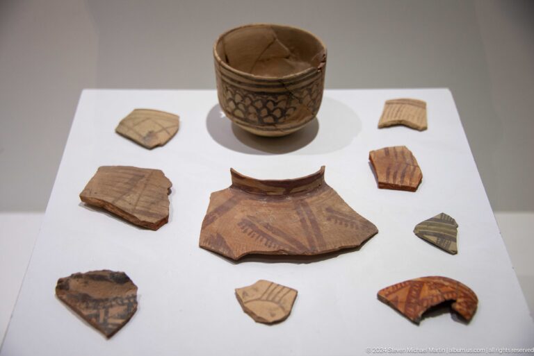 Reconstructed decorated bowl from Sarazm surrounded by incised and painted pottery fragments arranged on a flat surface.