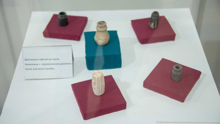 Small beads, seals, and other miniature archaeological objects from Sarazm displayed on separate colored blocks.