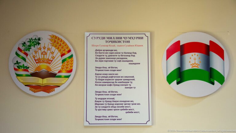 Wall-mounted official plaque flanked by Tajik flags and national emblems at the Sarazm museum in Tajikistan.