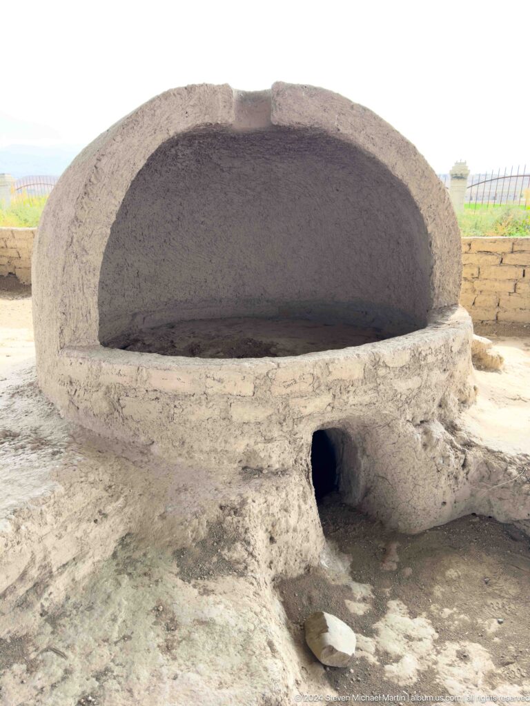 Close view of a domed earthen installation, likely an oven or hearth, with a broad rounded chamber and a small opening in the lower front wall at Sarazm.