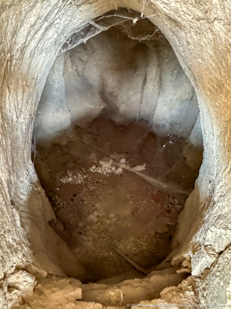 Top-down view into a circular, stone- or earth-lined pit at Sarazm with dark sediment at the bottom.