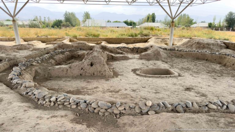 Circular and straight stone-lined foundations of ancient structures at Sarazm under a protective shelter.