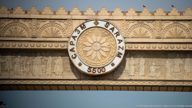 Close view of a circular Sarazm 5500 emblem with the word SARAZM, the number 5500, and a central stylized sun or flower design on a decorated wall.