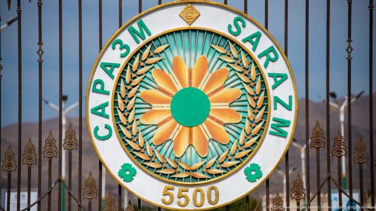 Colorful circular Sarazm 5500 emblem in green, orange, and turquoise mounted on a metal entrance gate.
