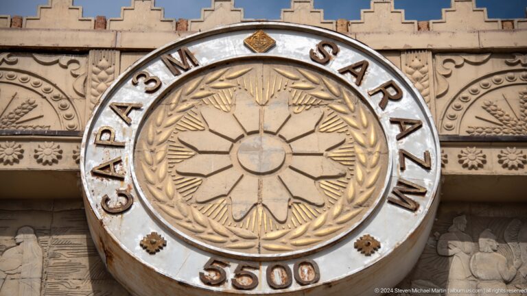 Close view of a circular stone medallion reading SARAZM with a central radial rosette motif on an entrance facade.