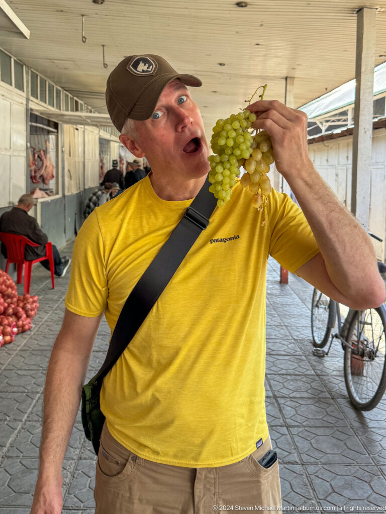 Male traveler eating grapes beside a bicycle.