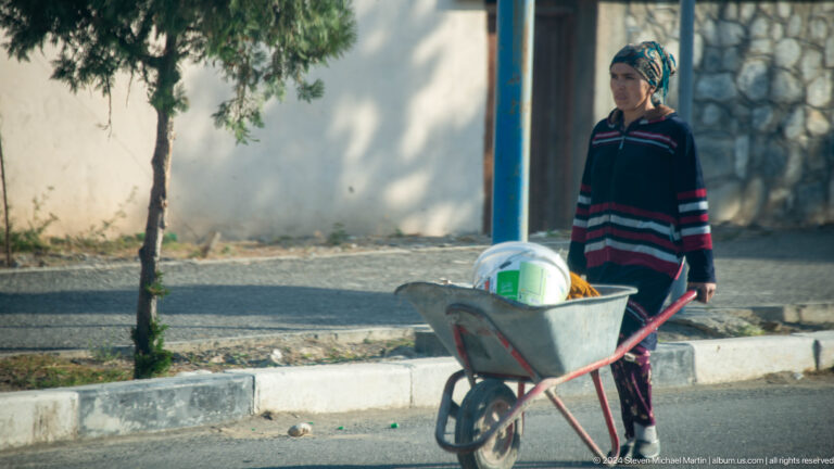 Man pushing a wheelbarrow beside a roadside water channel.