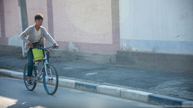 Older man riding a bicycle along a curb.