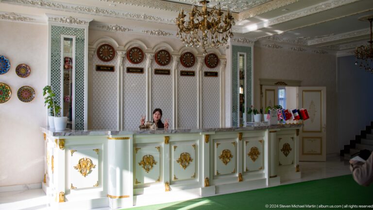 Ornate white-and-gold reception desk beneath chandeliers.