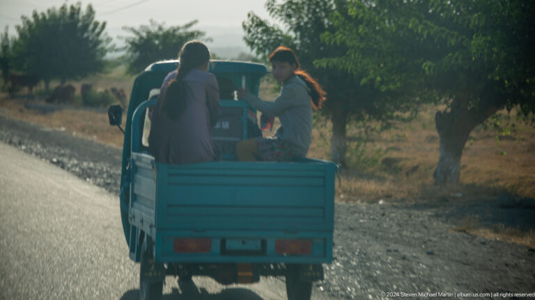 Passengers riding in the open bed of a small blue truck.