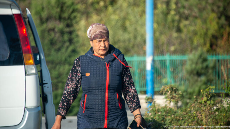 Older woman standing beside a parked vehicle.