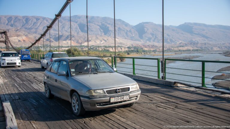 Car crossing a bridge with mountain valley beyond.