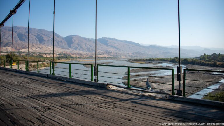 Bridge railing overlooking a broad river and mountains.