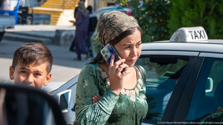 Woman speaking on a mobile phone beside a taxi.