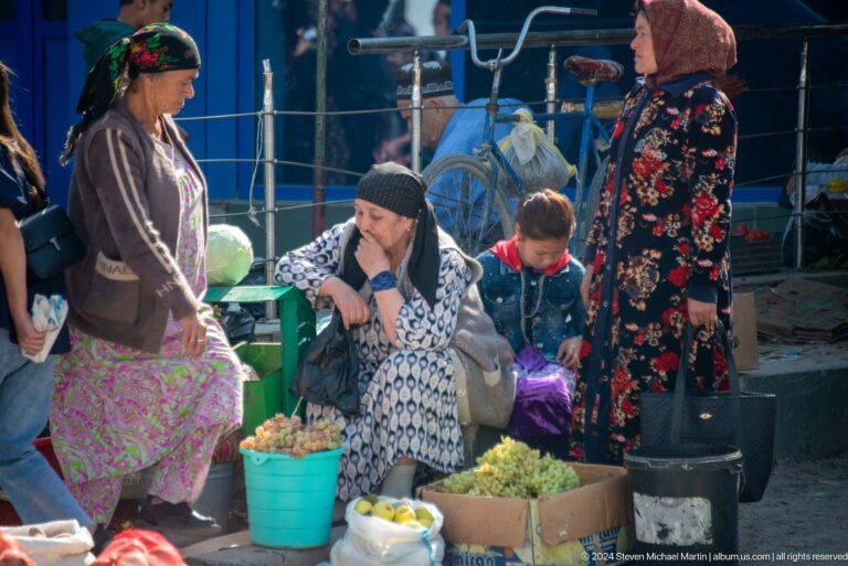 Woman vendor seated among buckets and market goods.