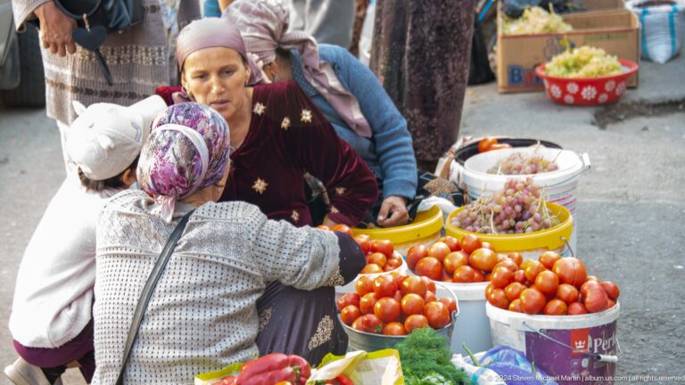 Women selecting tomatoes at an outdoor stall.