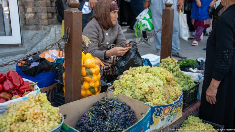 Vendor sorting grapes beside crates of fruit.