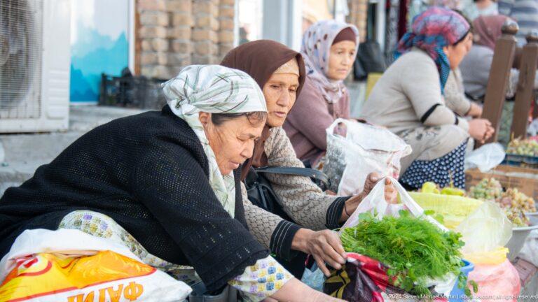 Women selling leafy greens at a market table.