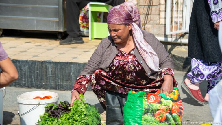 Woman vendor arranging tomatoes and green vegetables.