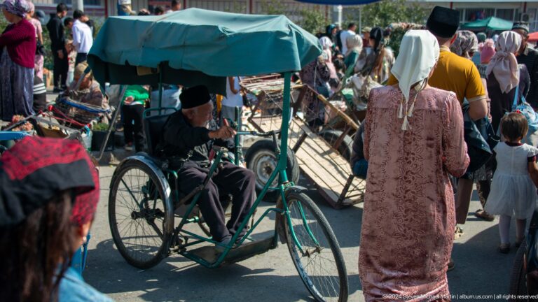Three-wheeled cycle rickshaw in a crowded market lane.